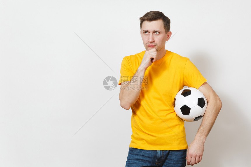 受启发的年轻沉思的欧洲男子球迷或身穿黄色制服的球员拿着足球图片