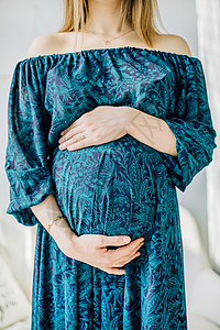 拿着她的肚子的蓝色礼服的孕妇图片