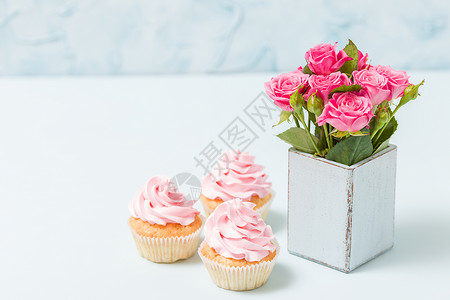蛋糕与粉红色奶油装饰和蓝色复古破旧别致花瓶中的粉红色玫瑰图片