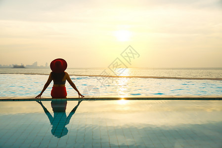 穿着大帽子的年轻女人在游泳池放背景图片