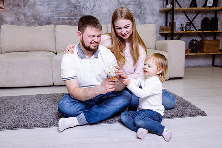 微笑着金发可爱的女婴和她的家人坐在沙发附近的地毯上家庭复图片