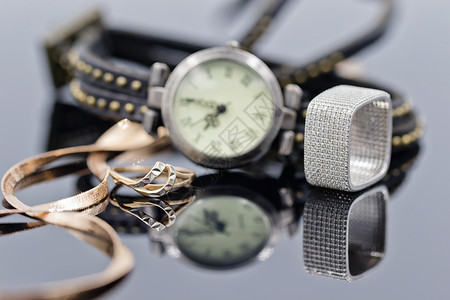 优雅的金戒指和链条位于带皮革表带的女士手表的背景上背景图片
