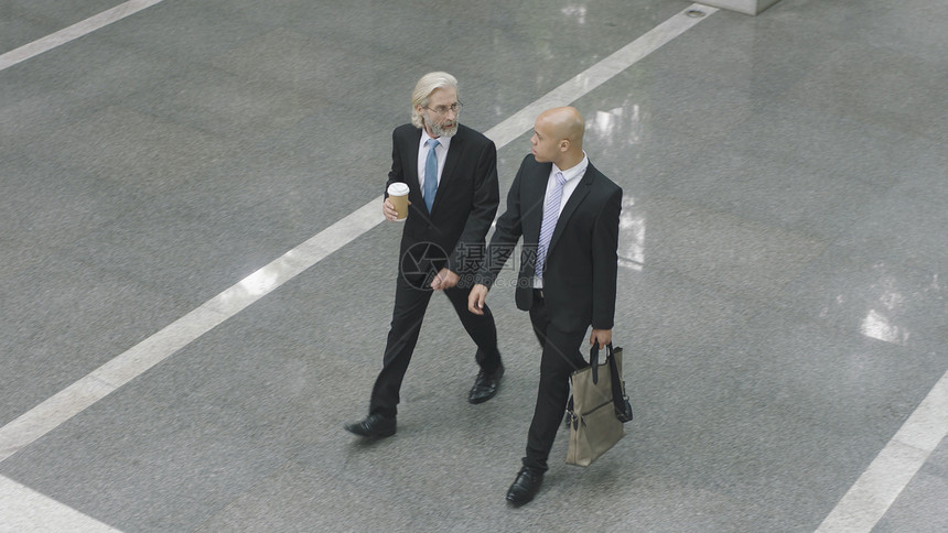 两个公司主管在走过现代办公大楼前厅时说话的高角度视角图片