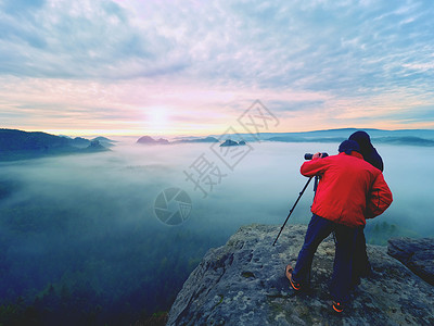摄影师用三脚架上的相机取景器留在悬崖上拍照图片