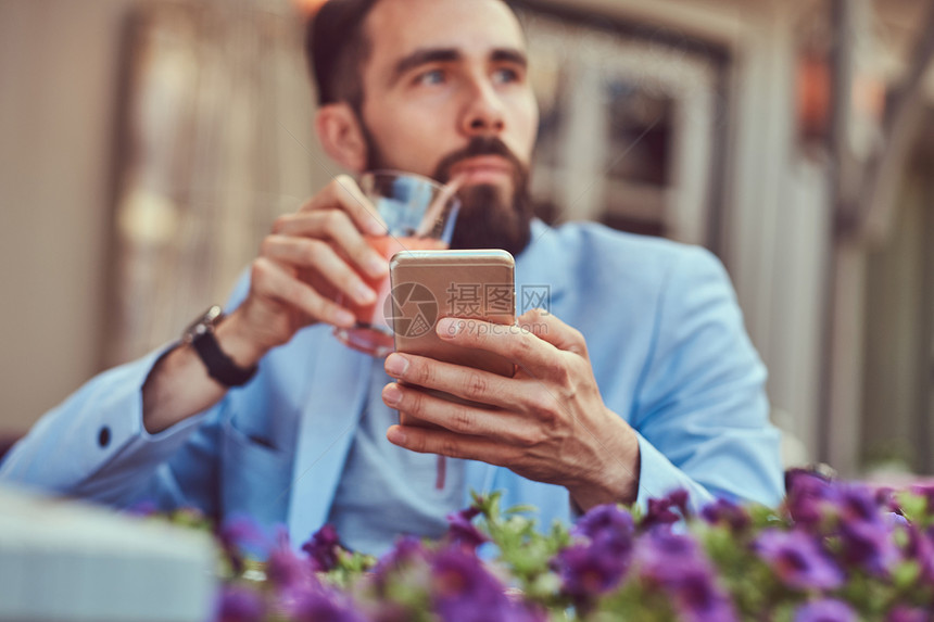 一个时髦的胡须商人的肖像理发时尚喝杯凉快的果汁拿着智能手机坐在图片