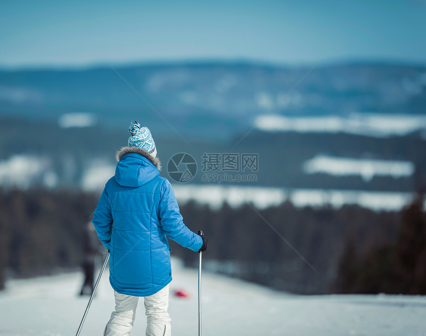 蓝夹克和羊毛帽的女滑雪者站在滑雪图片