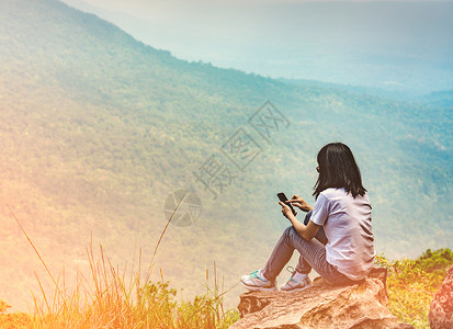 年轻的亚洲女坐在悬崖边的岩石上图片