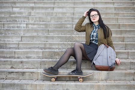 一个年轻的嬉皮士女孩骑着滑板女孩友带着滑板在城图片