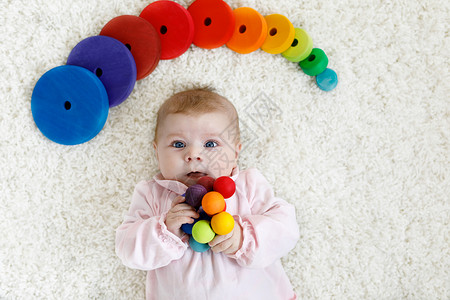可爱的新生婴儿在白色背景上玩彩色木制拨浪鼓玩具球图片