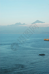 广阔的蓝色海湾让越南渔船相形见绌山在远处升起一排低洼的云层遮住了山脚图片