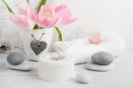 粉红色的郁金香鹅卵石和点燃的蜡烛白色木质背景图片