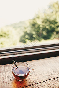 杯热茶在木桌上在窗光与山和天空的景色山顶上的美味饮料夏季旅行和旅行图片