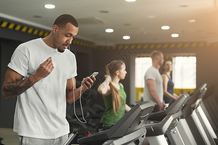 带着智能手机在健身房的跑步机上跑步图片