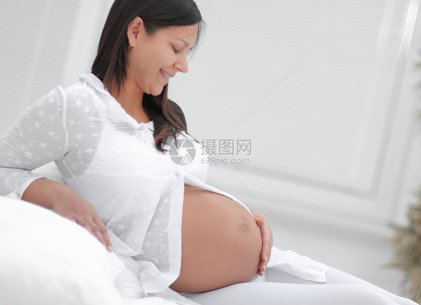 美丽的孕妇坐在沙发上手伸着腹部和复图片