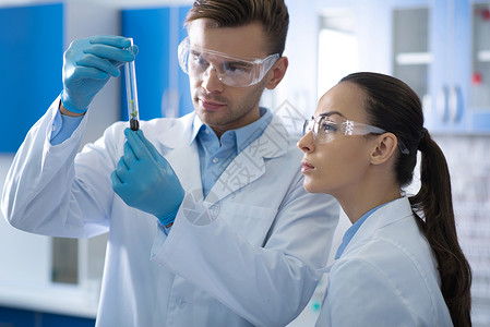 戴着眼镜和橡胶手套的年轻认真负责的科学家站在实验室里背景