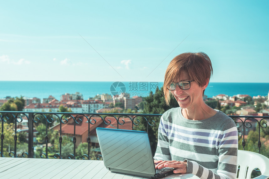 戴眼镜和休闲服装在户外露台上的笔记本电脑上工作的女人图片