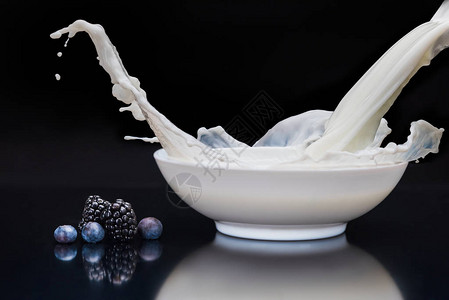 黑莓和蓝莓在白色碗里在黑色上倒牛奶背景图片
