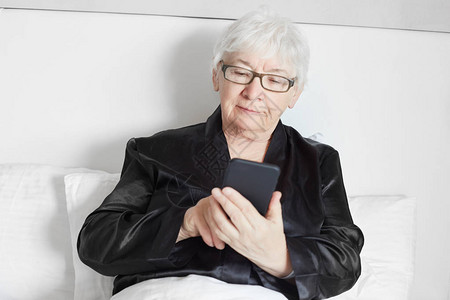 穿着黑色丝绸睡衣的老成熟女人在早晨的床上放松图片