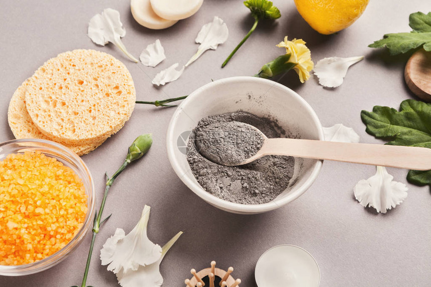 用各种护肤品在灰色背景下准备化妆品黑泥面膜在碗中干燥面部粘土粉用于家庭或沙龙水疗图片
