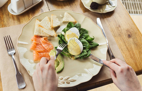 健康早餐荷包蛋配熏鲑鱼鳄梨菠菜和硬皮面包在餐厅或酒店享用早餐的图片
