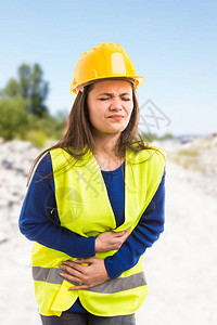 年轻女建筑师或工程师在户外场地背景下因胃痛和腹部疼痛作为图片