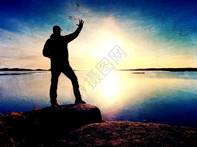年轻旅行者站在海面的石块上看太阳在寂静湾落基海图片