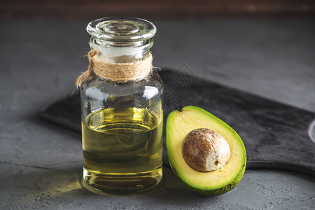 深色背景玻璃瓶中的绿色鳄梨果和油用于食品和美容程序的概念图片
