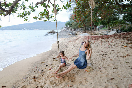 年轻美女与儿一起在海滩海边和沙滩上挥舞秋千图片