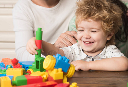 男婴看着由彩色积木制成的玩具结构孩子玩塑料砖轻木背景上带着笑脸的孩子图片