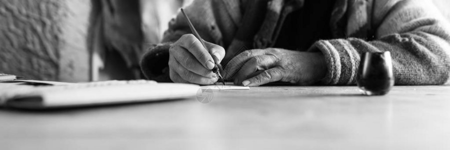一位老人在单色图像中使用笔尖和墨水在一张白纸上书写法背景图片