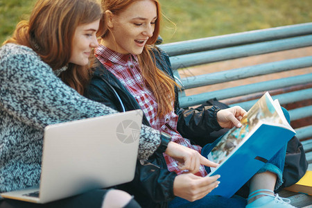 有吸引力的年轻成年女学生在户外的长凳上拿着书和笔记本电脑背景图片