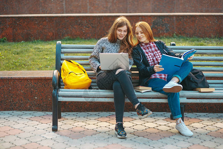 有吸引力的年轻成年女学生在户外的长凳上拿着书和笔记本电脑大学生网络计算机成瘾坐在校园外的长椅上说背景图片