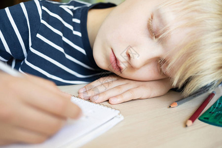 男孩在笔记本上做作业时睡在桌子上特写图片