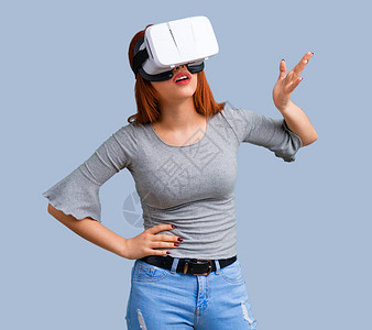 使用VR眼镜的年轻红发女孩蓝背景图片