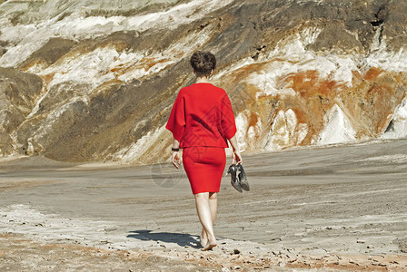穿着商业红礼服的女人脱下鞋子赤脚徒步走进荒漠的峡谷带着图片