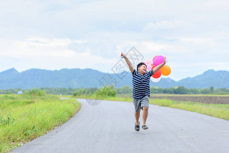 快乐的胖男孩带着气球在路上奔跑生活方图片