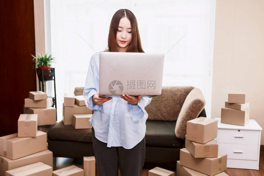 在家中携带手提笔记本电脑和纸板盒的年轻妇女商业在图片
