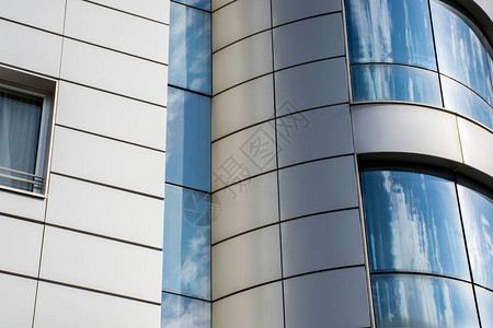 现代办公大楼细节玻璃表面窗户和金属外墙中的蓝云和天空的反射图片