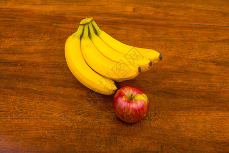 木桌上的一串香蕉和一个苹果背景图片