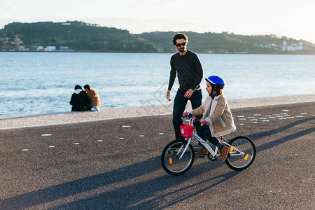 父亲与儿子在河岸骑自行车一图片