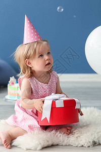 穿着生日派对礼帽的可爱小女孩和礼物盒坐在图片