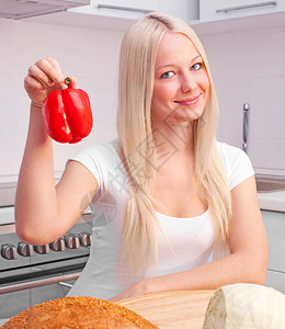 美丽的金发年轻美女在厨房吃胡椒图片