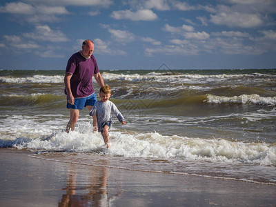 健壮的胡子爷和玩偶孙子穿着湿衣服在海滨上奔跑在海图片