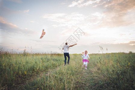 快乐的家庭爸和孩子在草地上奔跑在夏天与风筝在自然图片