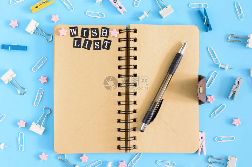 弹簧上的记事本是打开的文具旁边笔记本的棕色页面上刻有我的愿望清单蓝色背景图片