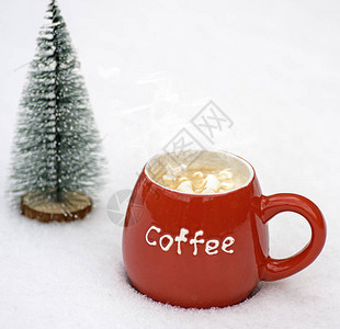 白色雪地上放着热咖啡和棉花糖片的红色陶瓷杯图片
