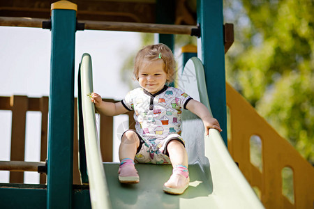 快乐的金发小蹒跚学步的女孩在户外操场上玩得开心和滑积极有趣的婴儿孩子微笑适合小孩的夏季休闲活动背景图片