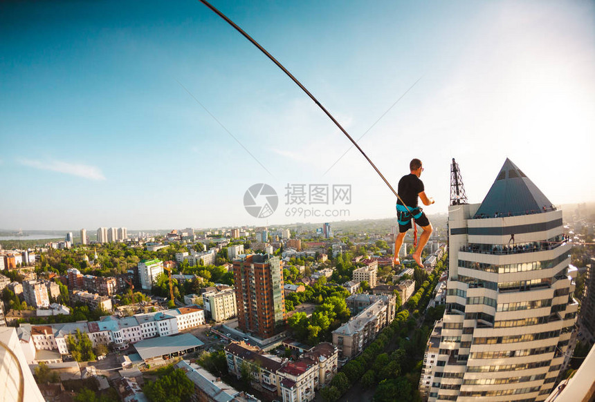 一个男人坐在两座建筑物之间的一条线上一个人在高处保持平衡城图片