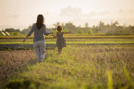 母亲和孩子通过在日落天空下田中行走来探索背景图片
