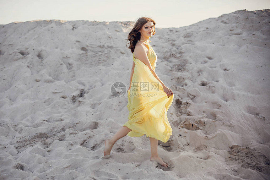 穿着黄色洋装的全身美女在湖边日光下沙滩上散步图片
